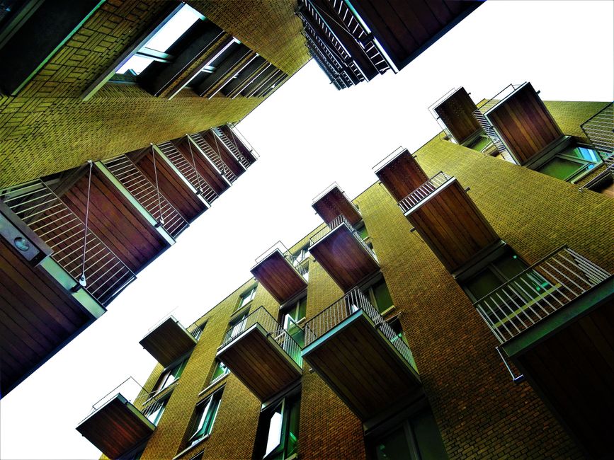 A multi-storey residential building with modern architectural design, featuring large glass balconies with metal railings on the left side, and white facade with several rectangular windows on the rig